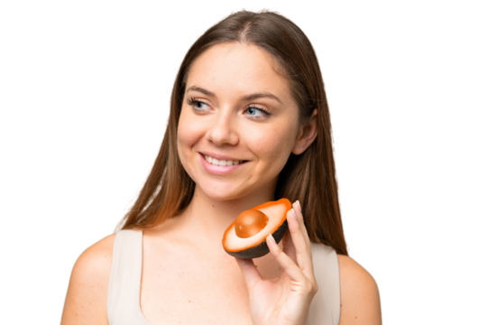 Young blonde woman over isolated chroma key background holding an avocado while smiling. Close up portrait