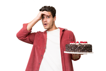 Young caucasian man holding birthday cake over isolated background doing surprise gesture while looking to the side