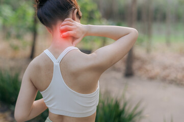 Asian woman experiencing neck pain after exercise, holding her neck with discomfort in outdoor...