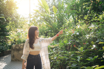 young woman enjoys serene walk in lush tropical garden, pointing at vibrant flowers under warm...