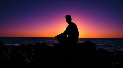 Silhouette of a young man sitting on rocks during a vibrant sunset.