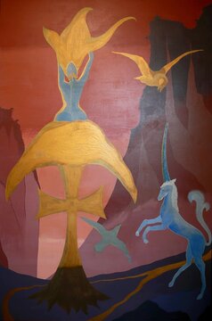 Oil and acrylic painting 182 x 120 of a blue female creature with golden hair perched on a golden cross on a mountain top against a setting sun, surrounded by gold and silver birds and a blue unicorn 
