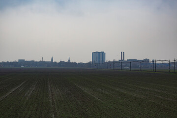 Landscape featuring a misty urban skyline alongside a plowed field during overcast weather in early spring