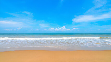 Fototapeta premium A vast sandy beach with gentle waves rolling in, under a bright blue sky with fluffy clouds
