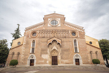 A frontal view of the Cathedral of Udine, Italy, showcasing its historic brick facade, arched...