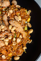 Wok noodles with chicken meat and sesame and peanut in bowl on dark stone background 
