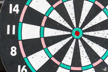 Detailed view of a well-used dartboard with colorful segments and a vibrant bullseye in a casual setting