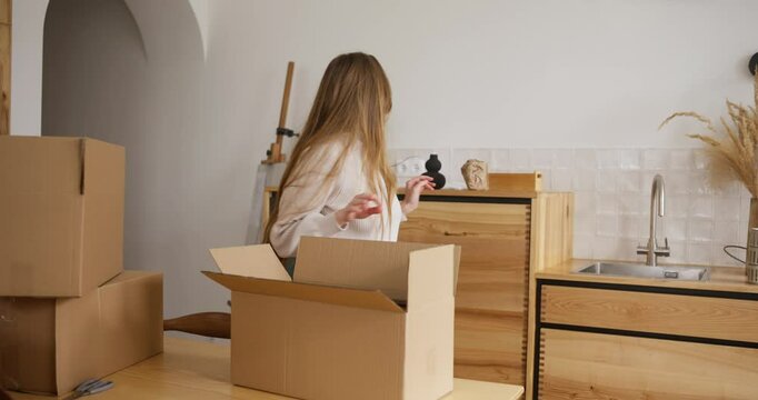 Focused blonde girl putting home decoration items into cardboard box while doing home moving