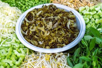Chopped sour pickled green mustard in white bowl with Various side dishes such as pickled vegetable, fresh salad and fruit for eat with main course of rice vermicelli, rice and curry of Thai food.