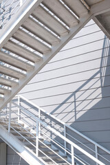 White metal fire escape on gray industrial warehouse building wall background in vertical frame, low angle view