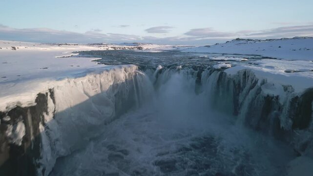 Aerial drone captures frozen selfless waterfall and river in snow-covered winter landscape in iceland