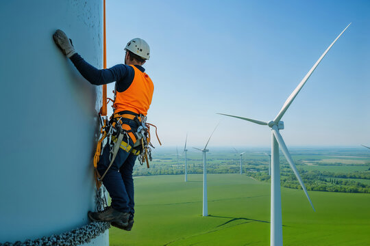 Engineer climbing wind turbine for inspection and maintenance in green field - Powered by Adobe