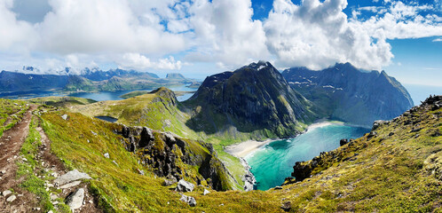 Panoramic view on the Lofoten mountains in Norway with two sandy bays in the foreground and multiple mountains, lakes and the sea in the background