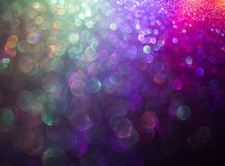 An out of focus, shallow depth of field photograph of a pale light multicolour abstract glittery surface, with vibrant neon light against a black background. Bokeh lights background