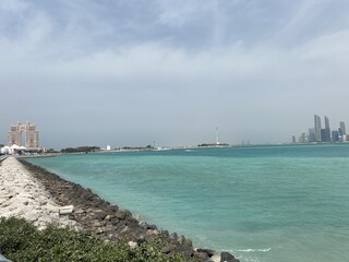 Coastal scene with clear turquoise waters and a rocky shoreline featuring a modern tower and spire ...