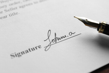 Fountain pen and signature on contract at wooden table, closeup