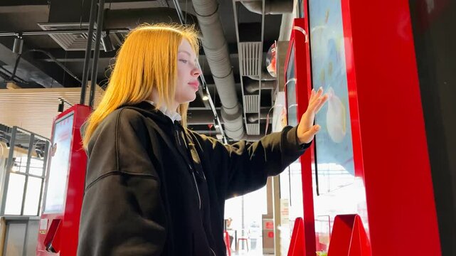 A young woman orders food on a self-service board in a fast food restaurant	
