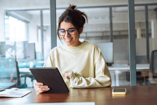 Smiling latina young professional business woman girl looking at pc device computer screen. Indian female businesswoman specialist holding digital tablet watching educational video at work in office