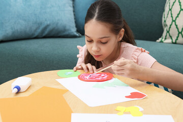 Girl applying glue onto paper figure for her creative project at table indoors. Art and craft