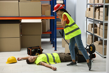 Accident at work. Worried woman and her unconscious colleague in warehouse
