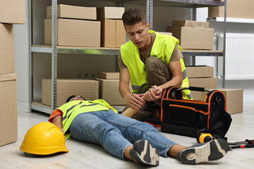 Accident at work. Man checking pulse of his unconscious colleague in warehouse