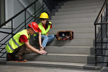 Accident at work. Man helping his injured colleague on stairs indoors