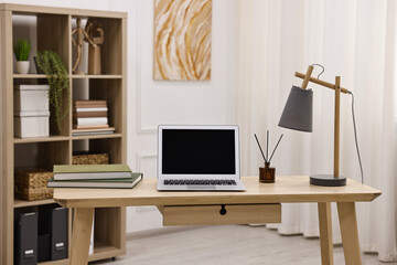 Comfortable workplace with modern laptop and lamp on wooden desk in home office