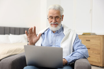 Fototapeta premium Bearded man having video chat via laptop in armchair indoors