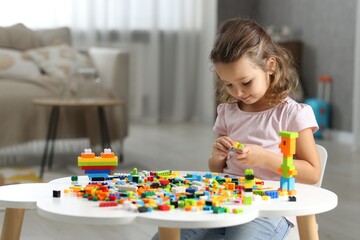 Cute girl playing with building blocks at white table indoors. Space for text