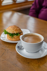 Top view of a breakfast scene featuring a flaky croissant sandwich filled with fresh greens and paired with a steaming cup of rich café crema. Cozy and elegant breakfast concept.