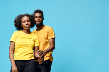 Obraz premium Young couple with Afro hairstyles in matching yellow shirts against a bright blue background, expressing love and joy in a modern urban style
