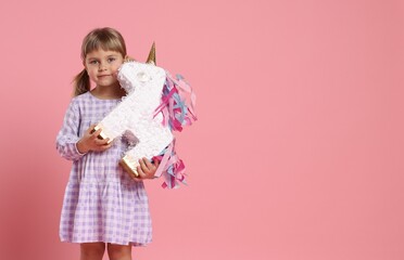 Cute girl with unicorn shaped pinata on pink background. Space for text