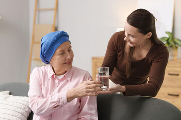 Caregiver giving water to woman with cancer indoors