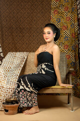 Fototapeta premium Elegant Indonesian woman wearing traditional batik fabric, sitting on a wooden bench. Vintage ethnic backdrop with rich patterns, cultural heritage, and graceful beauty in classic style.