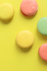 Bright French macarons on yellow background, top view. Assortment of multi-colored macarons with different flavors. Delicious pastries, flat lay. Food background. Sweets