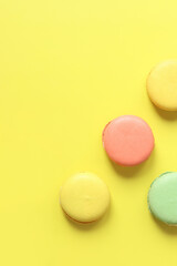 Bright French macarons on yellow background, top view. Assortment of multi-colored macarons with different flavors. Delicious pastries, flat lay. Food background. Sweets