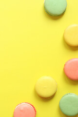 Bright French macarons on yellow background, top view. Assortment of multi-colored macarons with different flavors. Delicious pastries, flat lay. Food background. Sweets