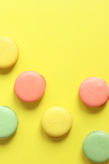 Bright French macarons on yellow background, top view. Assortment of multi-colored macarons with different flavors. Delicious pastries, flat lay. Food background. Sweets