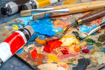 Old used brushes and palette knife in an artist's studio, palette with multi-colored spots of oil...