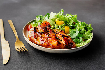 Aromatic homemade salad with cherry tomatoes, edamame beans, salad leaves and chicken breast with teriyaki sauce on black stone background close up, healthy diet food concept.