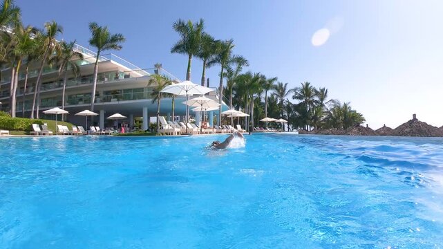 Rear view tracking shot of an older woman free crawl swimming in an outdoor pool, enjoying a relaxing sunny day. Active lifestyle concept for adults