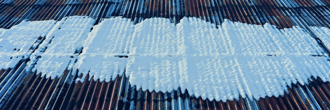 snow on rusty corrugated iron sheets of a barn roof