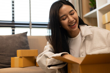 A woman is holding two boxes and smiling. She is sitting in front of a laptop. The boxes are brown and appear to be gifts. The woman seems happy and excited about the boxes
