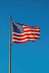 Fototapeta premium A soaring American flag against a clear blue sky with white clouds, suitable for patriotic events or national pride themes