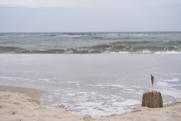 Sandcastle with Feather and Red plastic straw near Ocean Waves