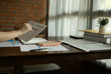 the businessman is sitting at a desk with a calculator and a stack of papers. She is looking at the...