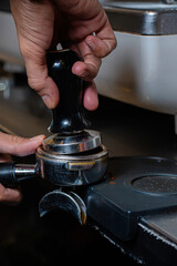 Barista holding coffee holder pressing coffee into holder for coffee machine, close up