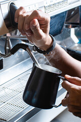Close up of the hands barista whips milk for espresso at the coffee machine in