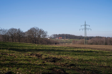 A field of grass with a power line tower with trees in the background.