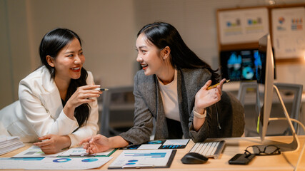 Two businesswomen discussing marketing strategy analyzing financial statistics data in office at night